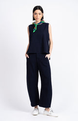 Woman wearing a navy sleeveless top and pants with a green scarf, standing against a white background.