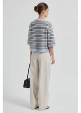 Woman wearing a striped sweater and beige pants on a light gray background
