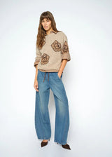 Woman wearing a beige sweater with floral patterns and blue jeans on a white background