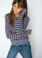 A woman wearing a maroon and light blue striped knit cardigan sweater with blue jeans, posing against a plain white background.