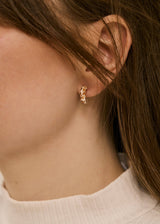 A close-up of a person's ear wearing a small gold huggie hoop earring with a textured, organic raised pattern.