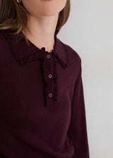 Close-up of a model wearing a dark plum long-sleeve top with a ruffled Peter Pan collar and a three-button placket.