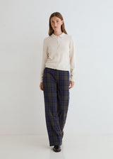 A woman modeling a cream long-sleeve button-up shirt and dark blue/black plaid trousers against a clean white studio background.
