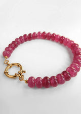 A beaded bracelet made of faceted pinkish-red gemstone beads with a gold clasp, photographed on a clean white background.