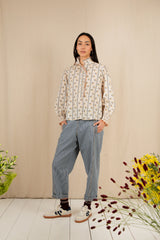 Person wearing a floral blouse and blue pants standing against a beige wall with flowers on the floor.