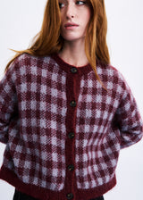 A woman wearing a fuzzy knit cardigan with a burgundy and white checkered pattern, dark buttons, and a ribbed crew neck, shown against a plain white background.