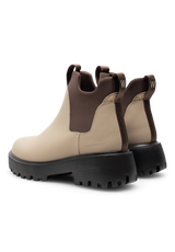 A pair of Chelsea-style ankle boots in beige and dark brown leather with a chunky black lug sole, shown from a rear three-quarter angle on a white background.