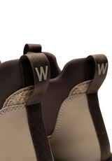 Close-up of the back of a pair of low-top sneakers in dark brown and beige, featuring pull tabs with a white 'W' logo and a textured beige insole.