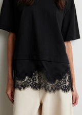 Person wearing a black top with lace trim and white pants against a plain background