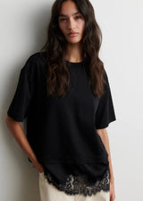 Woman wearing a black t-shirt with lace trim against a white background