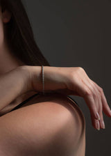 A close-up lifestyle shot of a woman's hand and shoulder wearing a delicate silver chain bracelet against a dark gray background.