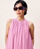 Person wearing a pink sleeveless dress and sunglasses on a plain background