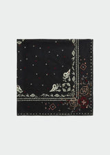 A square black bandana featuring a white paisley border and small red and white embroidered details, displayed flat against a light gray background.