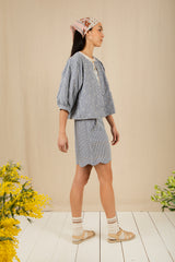 Woman wearing a light blue outfit with a matching headscarf, standing on a wooden floor with yellow flowers.