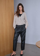 Woman wearing a beige cardigan and black pants standing against a gray wall.