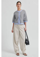 Woman wearing a striped cardigan and beige pants holding a black handbag on a light gray background