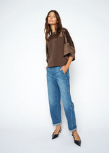 Woman wearing a brown top and blue jeans on a white background
