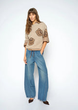Woman wearing a beige sweater with floral patterns and blue jeans on a white background