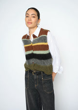 Person wearing a multicolored striped sweater vest over a white shirt with dark jeans on a white background