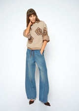Woman wearing a beige sweater with floral patterns and blue jeans on a white background