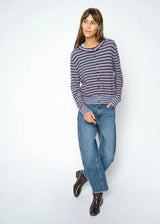 A woman modeling a long-sleeve knit cardigan with thin horizontal navy and burgundy stripes, paired with blue jeans and dark brown leather boots, against a light gray studio background.