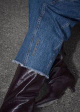 Close-up of blue jeans with a frayed hem on a dark surface