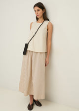 Woman wearing a sleeveless beige top and striped pants, standing against a white background.