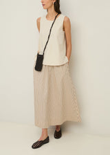 Woman wearing a sleeveless top and striped skirt with a black bag against a white background