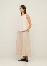 Woman wearing a white sleeveless top and beige striped skirt on a plain background