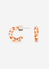 A pair of small hoop earrings with a giraffe print pattern in orange and brown on a white background, shown on a light gray studio background.