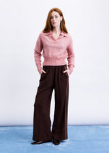 Woman wearing a pink sweater and brown pants on a white background