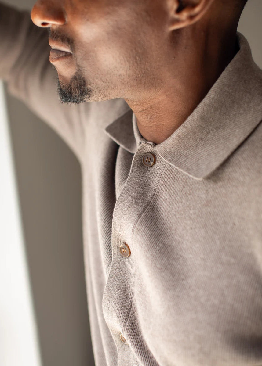 Close-up of a man wearing a light taupe knit polo shirt with brown buttons, shown in profile against a soft gray background.
