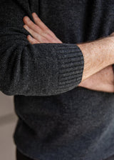 Close-up of a person wearing a dark charcoal gray ribbed knit sweater, with arms crossed.