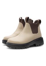 A pair of Chelsea-style ankle boots in beige and dark brown leather with chunky black lug soles, shown on a clean white background.