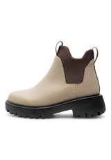 A single ankle-height Chelsea-style boot in light beige leather with a dark brown elastic side panel and a chunky black lug sole, shown in side profile on a white background.