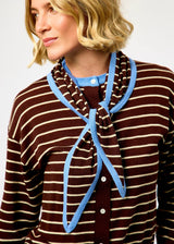 A close-up of a woman wearing a brown and cream striped knit top with a light blue knotted scarf or necktie detail.
