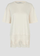 An off-white short-sleeve tunic top with a round neckline and a decorative lace hem, shown against a light gray background.