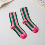 Green and pink striped socks with heart-shaped toes on a light surface.