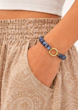 Person wearing a blue beaded bracelet with a gold clasp on a neutral background
