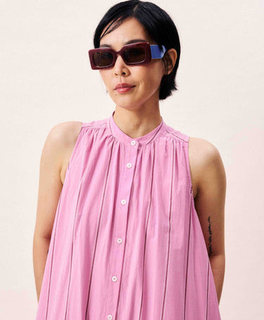 Person wearing a pink sleeveless dress and sunglasses on a plain background