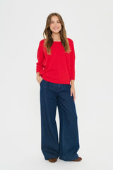 Woman wearing a red sweater and blue jeans on a white background