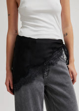 A close-up of a person wearing a black wrap-style top with sheer lace trim over gray jeans and a white tank top, shown against a plain light background.